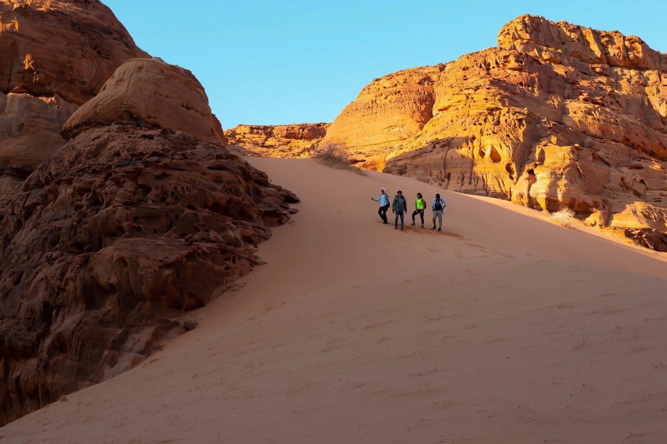 Hikers walking dunes for desert sandboarding in AlUla